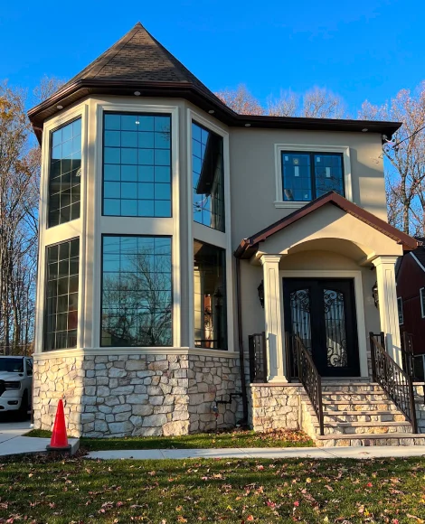 Two-story modern house with large, tinted floor-to-ceiling windows, stone veneer base, wrought iron front door, and a steeply pitched turret-style roof on one side.