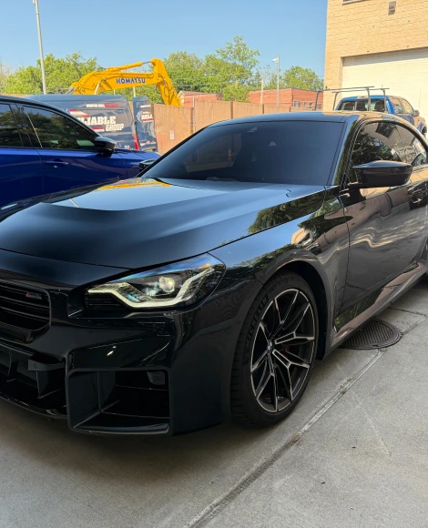 Sleek black BMW M-series sedan with dark tinted windows and gloss black wheels, parked outside an automotive shop.