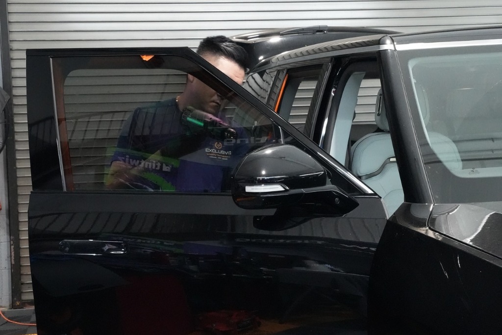 An installer from Exclusive Window Tinting NYC works on a black SUV’s front window inside their Staten Island shop, illustrating the range of services that influence car window tint cost in Staten Island including film type and vehicle coverage.