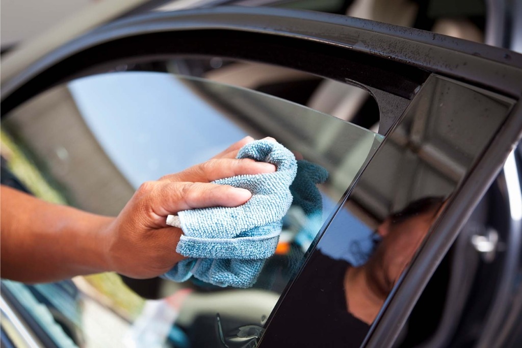 A person uses a soft microfiber cloth to gently clean a car window, illustrating proper window tint maintenance recommended by Exclusive Window Tinting NYC in Staten Island, NYC to preserve film clarity and durability.