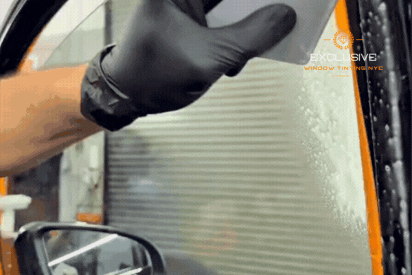 Close-up of a gloved technician from Exclusive Window Tinting NYC in Staten Island using a squeegee to apply film smoothly to a car window, demonstrating the quality and precision of professional tint installation.